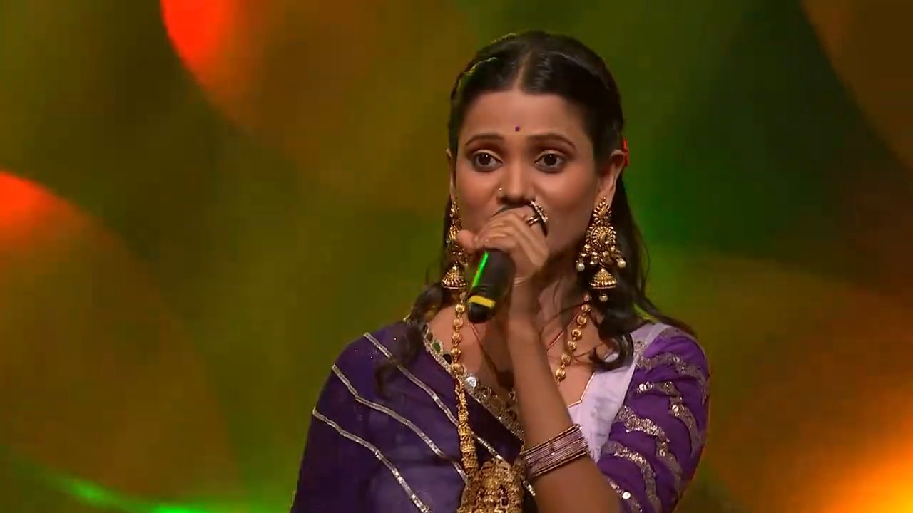 Barnali Hota singing on stage in a purple saree
